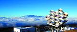 The second phase of AMiBA consisting of thirteen 1.2m antennas was completed at the end of 2009. The 13-element array, with improved resolution and sensitivity, can be effectively study clusters that are much further away from us. Scientific operations resumed in 2011. The background shows another volcanic peak, Mauna Kea.